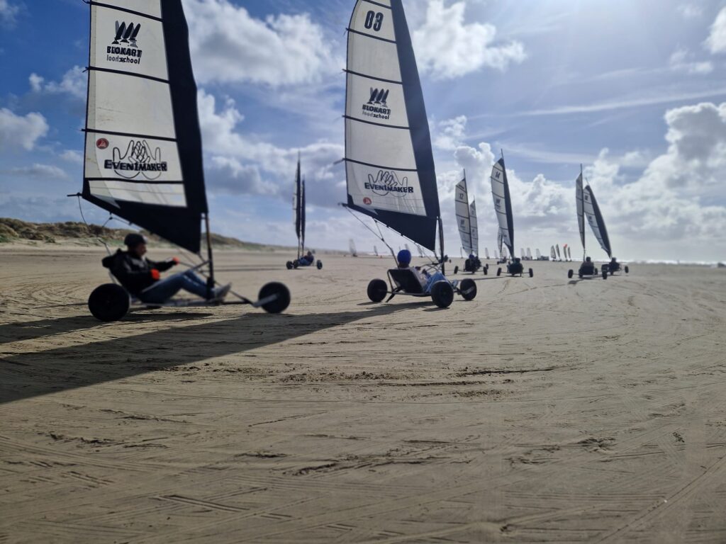 Groep mensen blokartend op het strand van IJmuiden met snelle strandzeilers en zee op de achtergrond