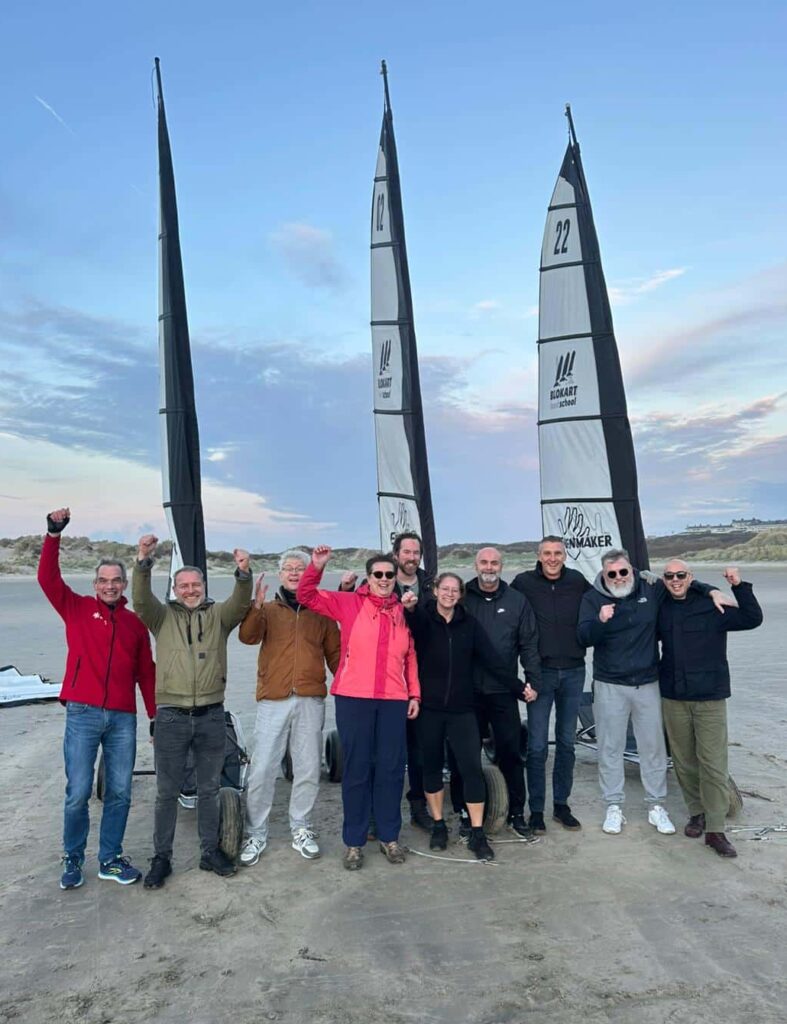 Groep collega’s juichend op het strand van IJmuiden na een geslaagd bedrijfsuitje blokarten